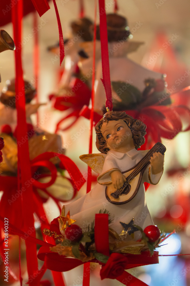 Naklejka premium Christmas angel with red ribbon. Christmas toys at the fair. Festive market in Europe. Christmas decoration concept. Cute angel doll. Christmas shopping. Winter holidays concept. Magic atmosphere.