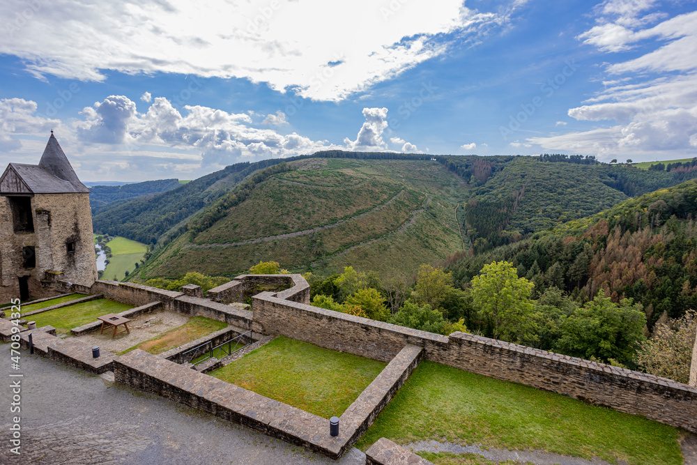 Landscape seen from the upper courtyard of the medieval castle of Bourscheid, ramparts, tower and valley, mountains, green trees, dramatic blue sky with abundant clouds in the background, Luxembourg