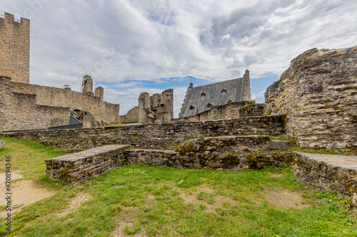 Open-air ruin at the medieval castle of Bourscheid, dilapidated stone walls, stairwell, courtyard with the roof of the Stolzembourg house in the background, cloudy day in Luxembourg