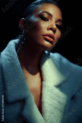 Closeup portrait of an elegant and beautiful african american young woman with perfect smooth glowing skin, full lips and fashionable makeup. Dark background. Studio shoot
