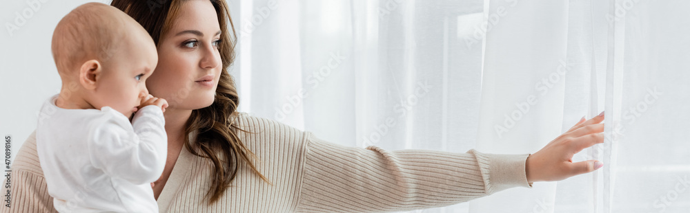 Young body positive mother holding baby near curtains at home, banner. Young body positive mother holding baby near curtains at home, banner.