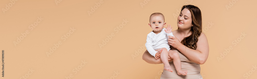 Smiling mother holding baby daughter waving hand isolated on beige, banner. Smiling mother holding baby daughter waving hand isolated on beige, banner.