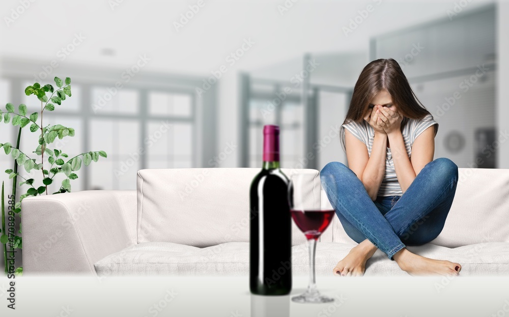 Sad crying despaired young lady suffering from stress, grief and difficulties with bottle of wine