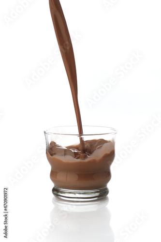 Pouring chocolate drink into a transparent glass isolated in a white background with reflection