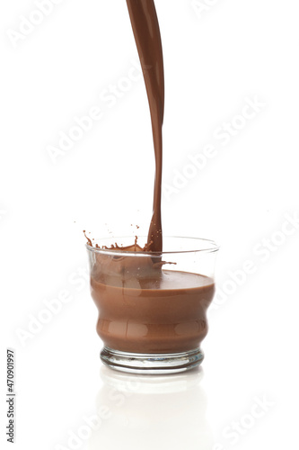 Pouring chocolate drink into a transparent glass isolated in a white background with reflection