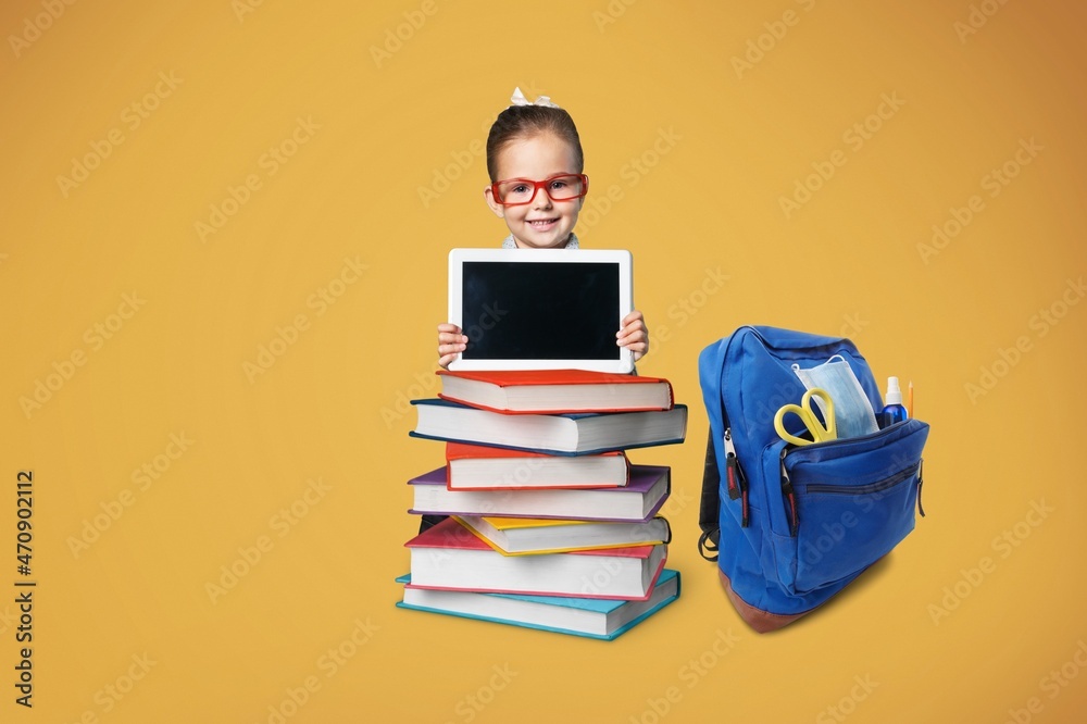 Smiling caucasian school child sitting behind the stack of book shows the tablet Smiling caucasian school child sitting behind the stack of book shows the tablet