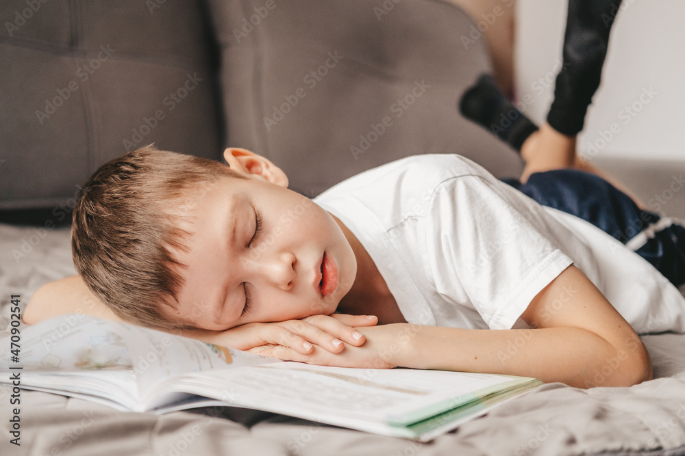 portrait of a boy who fell asleep during homework lying on the couch. Teenager over a notebook, on the bed. Homeschooling a 9 year old boy. Difficult study portrait of a boy who fell asleep during homework lying on the couch. Teenager over a notebook, on the bed. Homeschooling a 9 year old boy. Difficult study