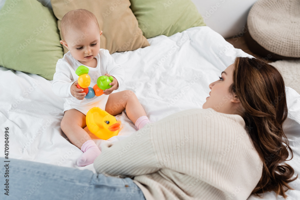 Plus size mother lying near baby daughter with toys on bed. Plus size mother lying near baby daughter with toys on bed.