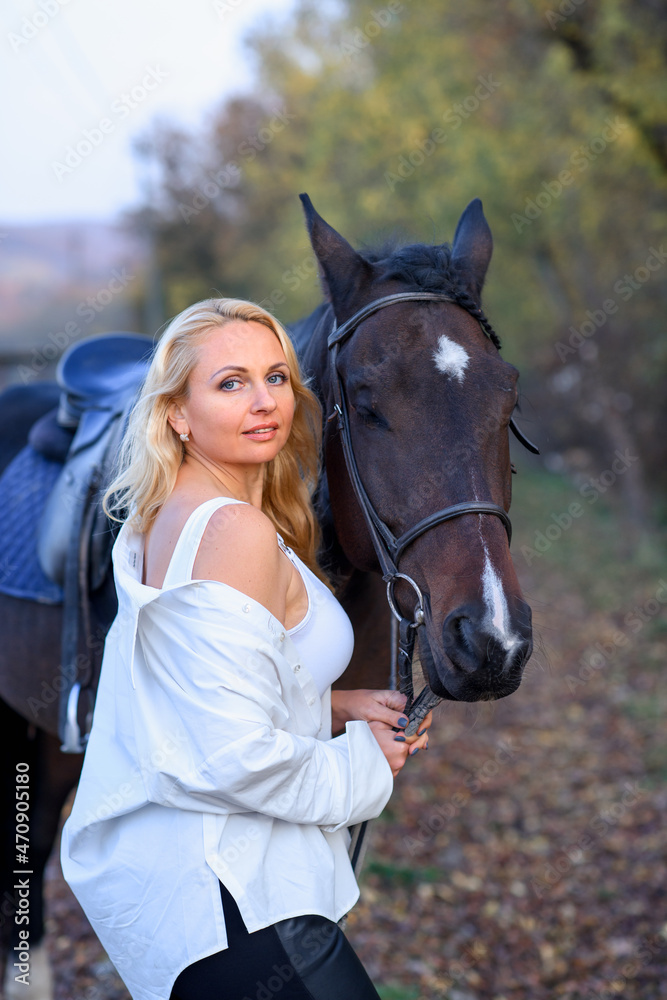 Obraz premium beautiful caucasian girl in a white shirt with a horse in the forest at sunset
