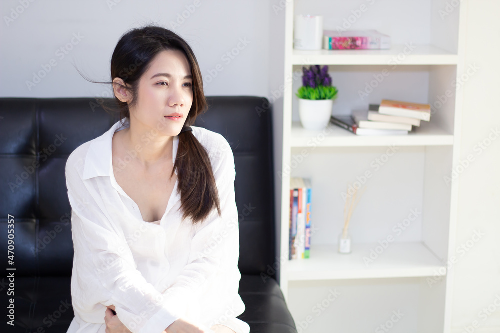 Asian beautiful woman who wear white shirt is sitting in living room to relax and rest on holiday or weekend. a Day dreaming.