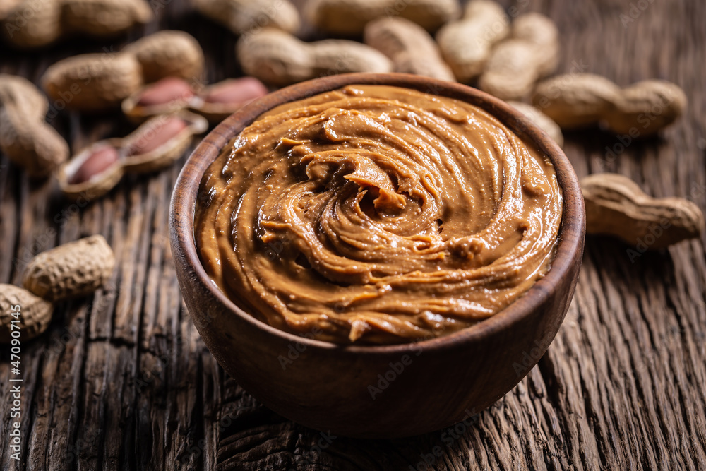 Peanut butter in wooden bowl and peanuts on rustic oak table Peanut butter in wooden bowl and peanuts on rustic oak table