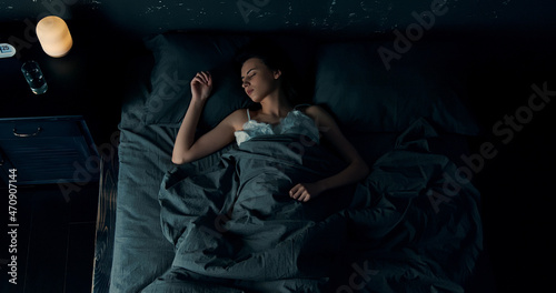 Top view of beautiful young woman sleeping cozily in bed. Lady lying sound asleep at night. Loft interior.