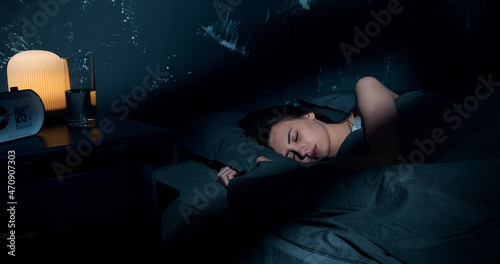 Beautiful young brunette woman sleeping on side, lying cozily in bed, hugging a pillow. Lady sound asleep at night. Loft interior. photo