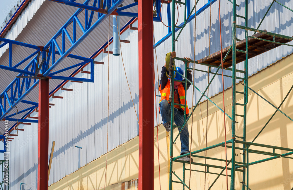 Fototapeta premium Construction worker with safety workwear climbing on scaffolding for working on roof warehouse structure in construction site