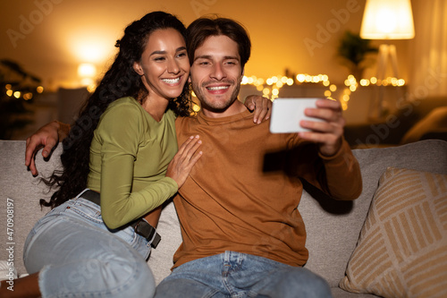 Young Couple Making Selfie On Phone Hugging Sitting At Home