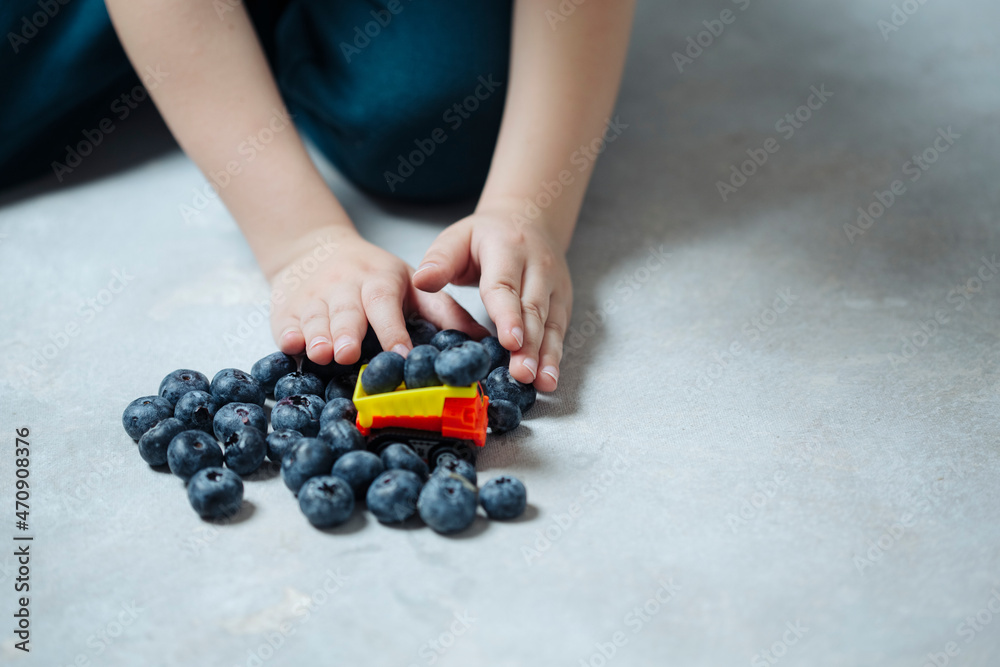 Fototapeta premium Transportation of fresh juicy blueberries for a customer, a boy plays on the floor in a typewriter. the concept of delivery and supply of healthy food to the population.