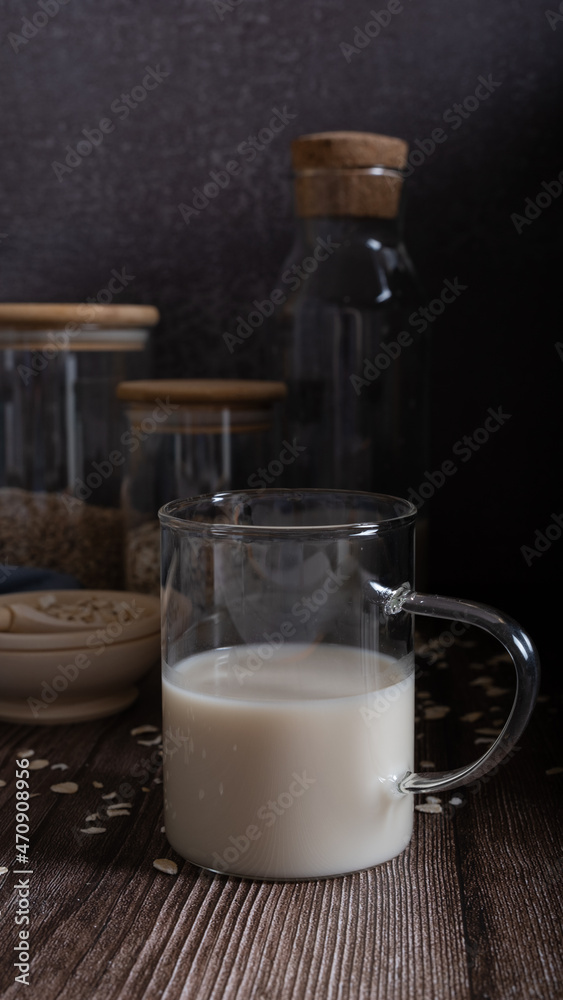 Oat milk in a glass glass with cans of oat flakes and grain on a dark background. Low key Oat milk in a glass glass with cans of oat flakes and grain on a dark background. Low key
