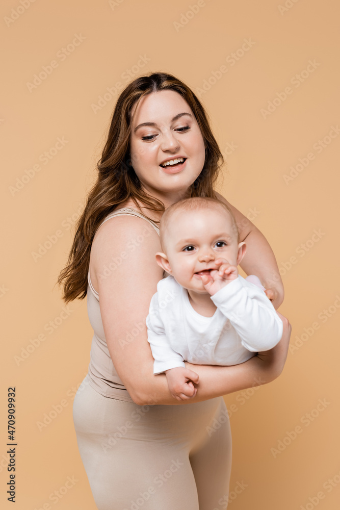 Smiling plus size mom holding positive baby daughter isolated on beige. Smiling plus size mom holding positive baby daughter isolated on beige.