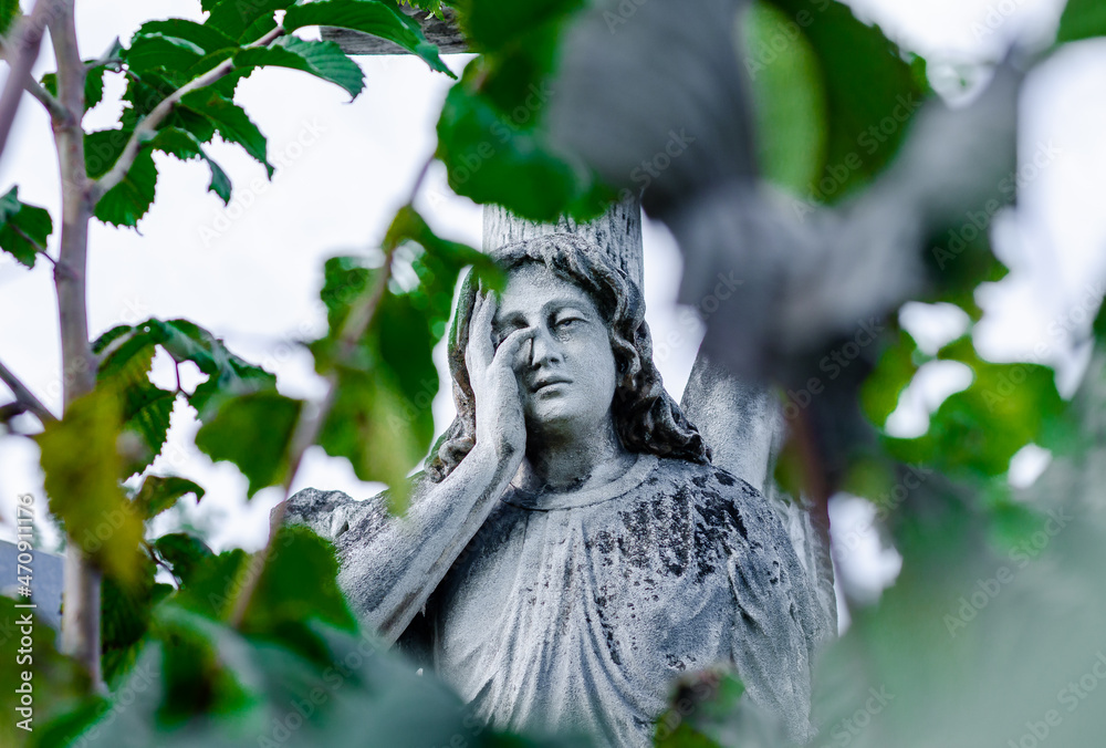 Old statue of weeping stone angel on background of green leaves. Old statue of weeping stone angel on background of green leaves.