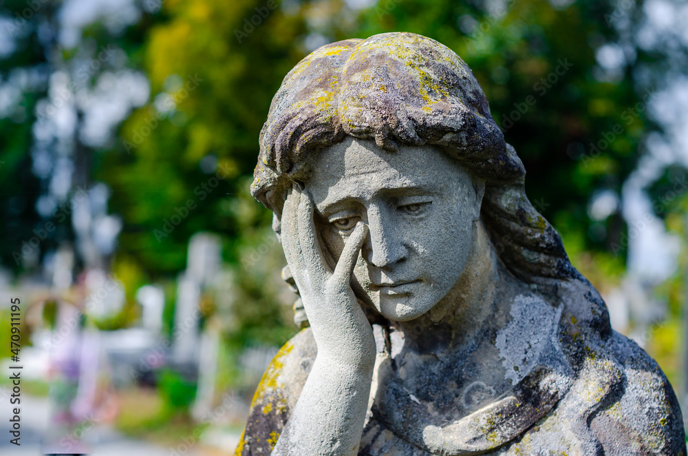 Old stone statue in the cemetery. Sad stone woman.
