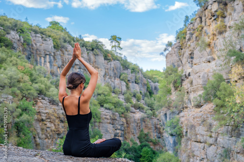 Young female doing lotus pose while sitting on edge of rocky cliff in highlands during yoga training in nature