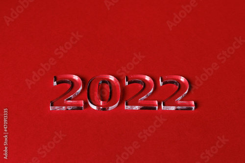 Photo of numbers 2022 made of volumetric transparent acrylic glass on a red background. Selective focusing.