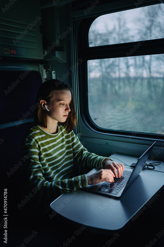 Naklejka premium Attractive woman rides in a train in the evening and looks at the laptop screen with a serious face. Freelancer working on a computer on a train