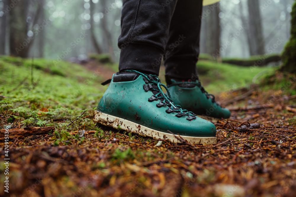 Man in green boots stands on the wet ground with moss in the mountain forest on a hike. Close photo of hiking boots.