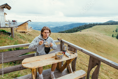 Young man eating pasta for breakfast on the terrace of a wooden house in the mountains. Tourist eating in the mountains