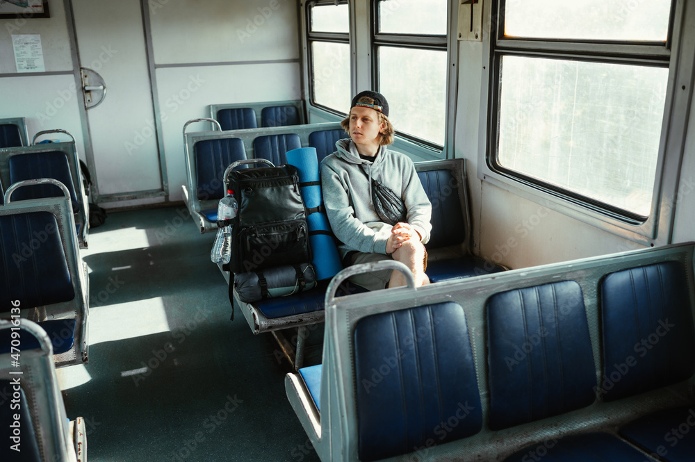 Guy tourist in casual clothes travels in an empty train with a backpack and looks away. Guy tourist in casual clothes travels in an empty train with a backpack and looks away.