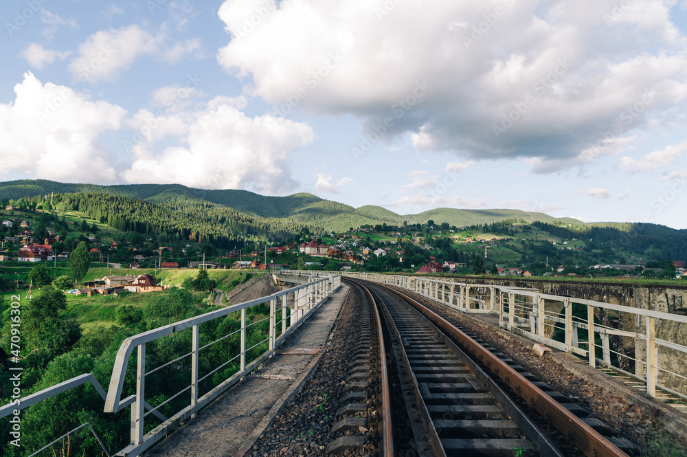 Railway track on the bridge on the background of a beautiful mountain landscape. Suburban railway on the background of the village and mountains. Vorokhta. Ukraine, Carpathians Railway track on the bridge on the background of a beautiful mountain landscape. Suburban railway on the background of the village and mountains. Vorokhta. Ukraine, Carpathians