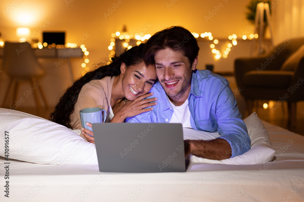 Spouses Watching Film On Laptop Lying In Bed At Home