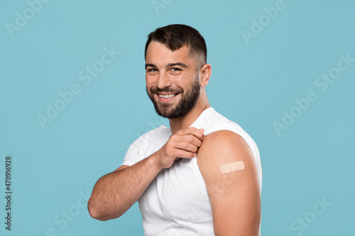 Smiling adult attractive caucasian guy show shoulder with band aid after vaccination photo