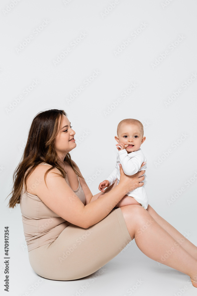 Pretty plus size woman holding child with finger near mouth on grey background. Pretty plus size woman holding child with finger near mouth on grey background.