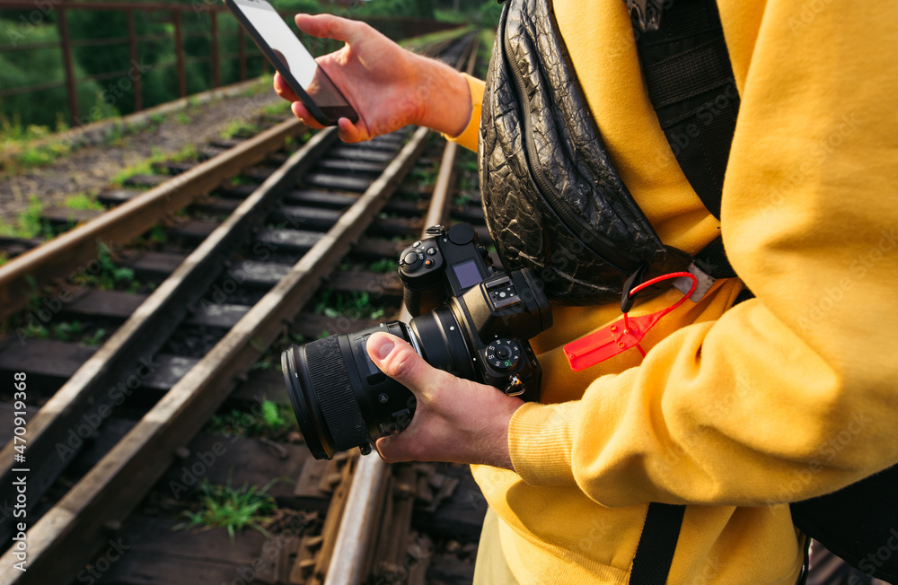 Male tourist holds a camera in his hands and uses a smartphone on the background of the railway track, close-up photo.