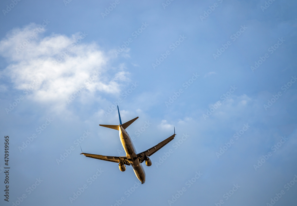 Flying plane against the blue cloudy sky before landing with the landing gear released