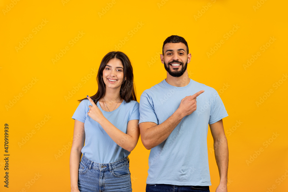 Portrait of excited arab man and woman pointing fingers aside at free space and smiling to camera over yellow background Portrait of excited arab man and woman pointing fingers aside at free space and smiling to camera over yellow background