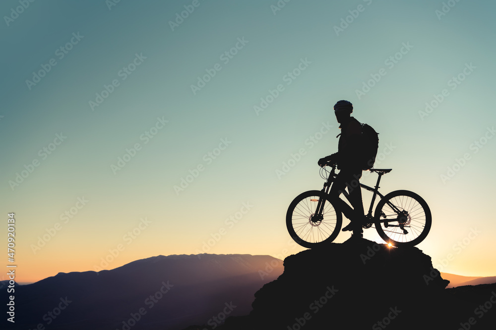 Cyclist's silhouette on big rock against sunset