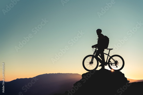 Cyclist's silhouette on big rock against sunset