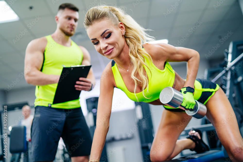 Fototapeta premium Young pretty lady working out in the gym with trainer. Female sporty woman in sportswear.