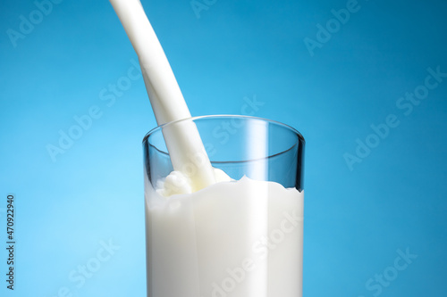 Pouring milk splash in a glass over blue background.