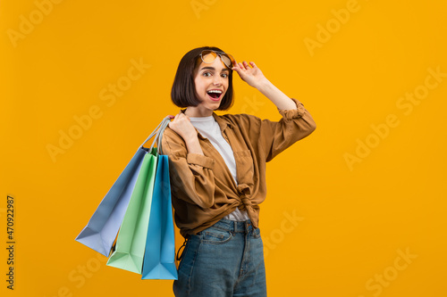 Special big holiday sales. Joyful woman wearing sunglasses and holding colorful shopping bags, yellow background