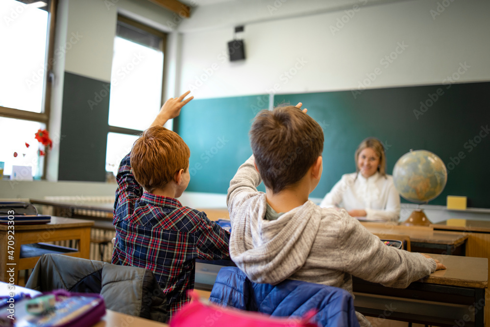 Obraz premium Schoolchildren at classroom with raised hands answering teacher's question.