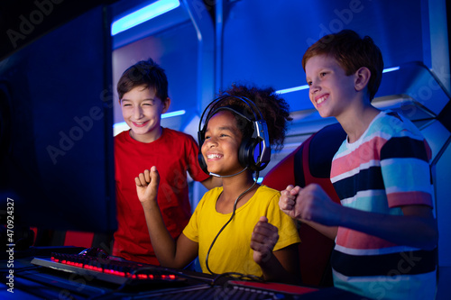 Fotografiet Cheerful kids at game room playing favorite video game and supporting female gamer