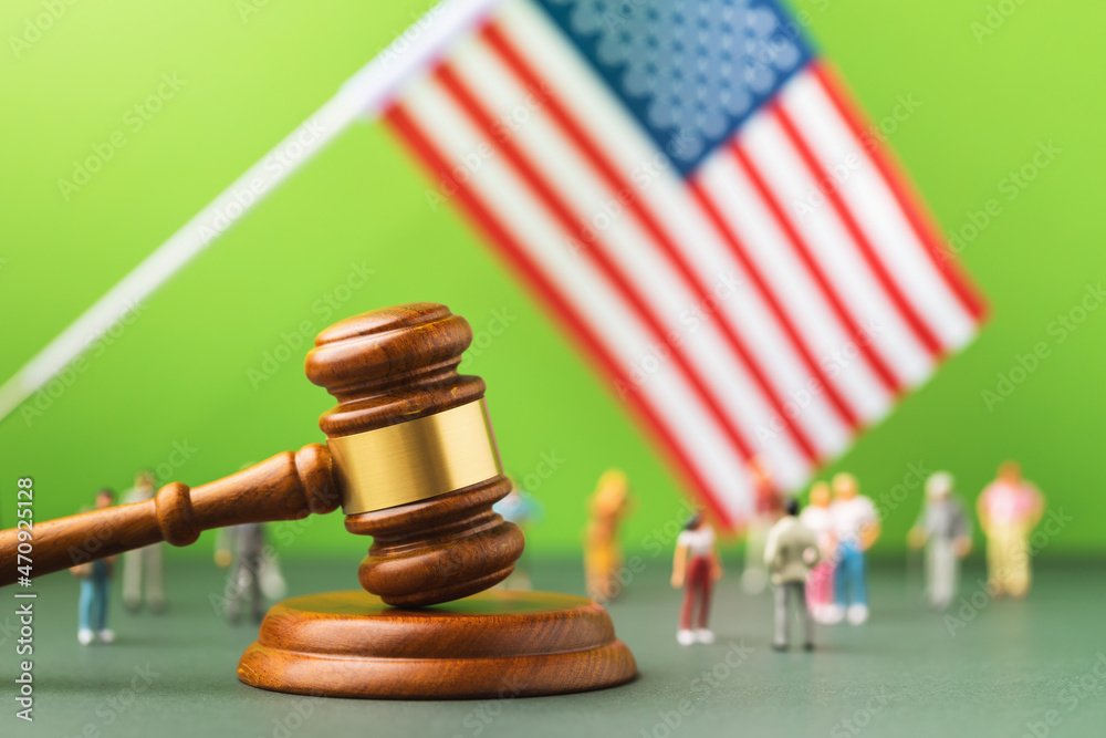 Judge gavel against the background of the blurred flag of the United States of America and plastic toy men, the concept of litigation in the American Society