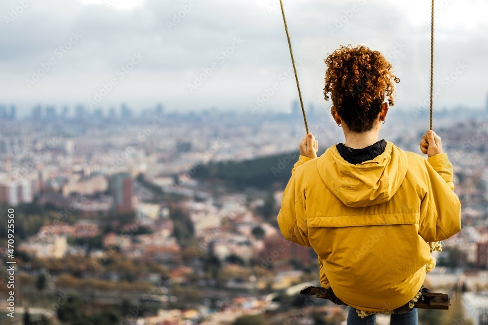 Chica con chaqueta amarilla columpiandose y skyline de Barcelona