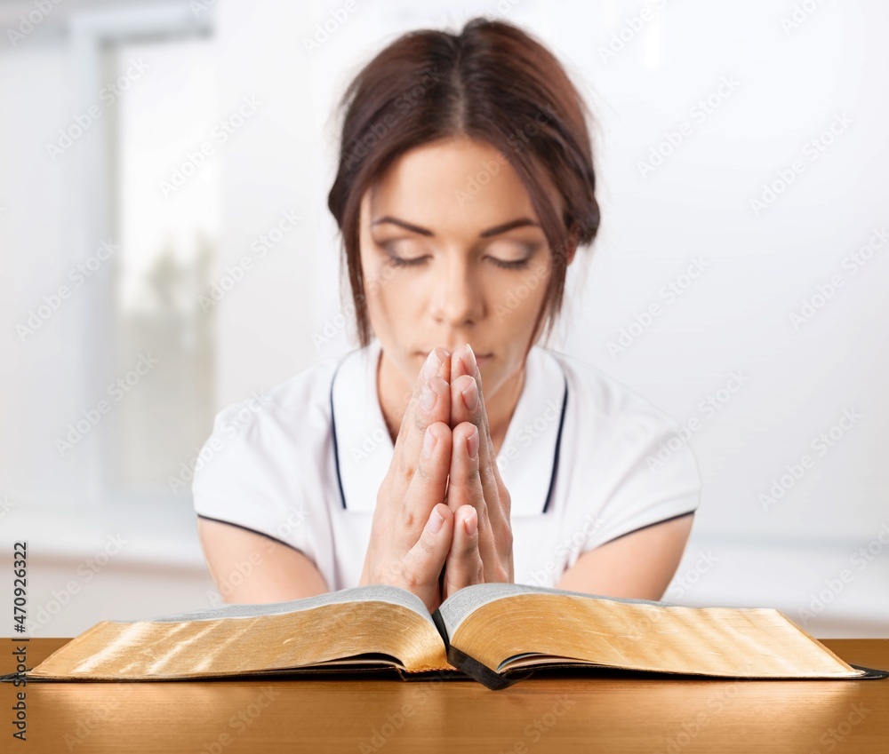 Religious young woman praying over Bible book at table indoors Religious young woman praying over Bible book at table indoors