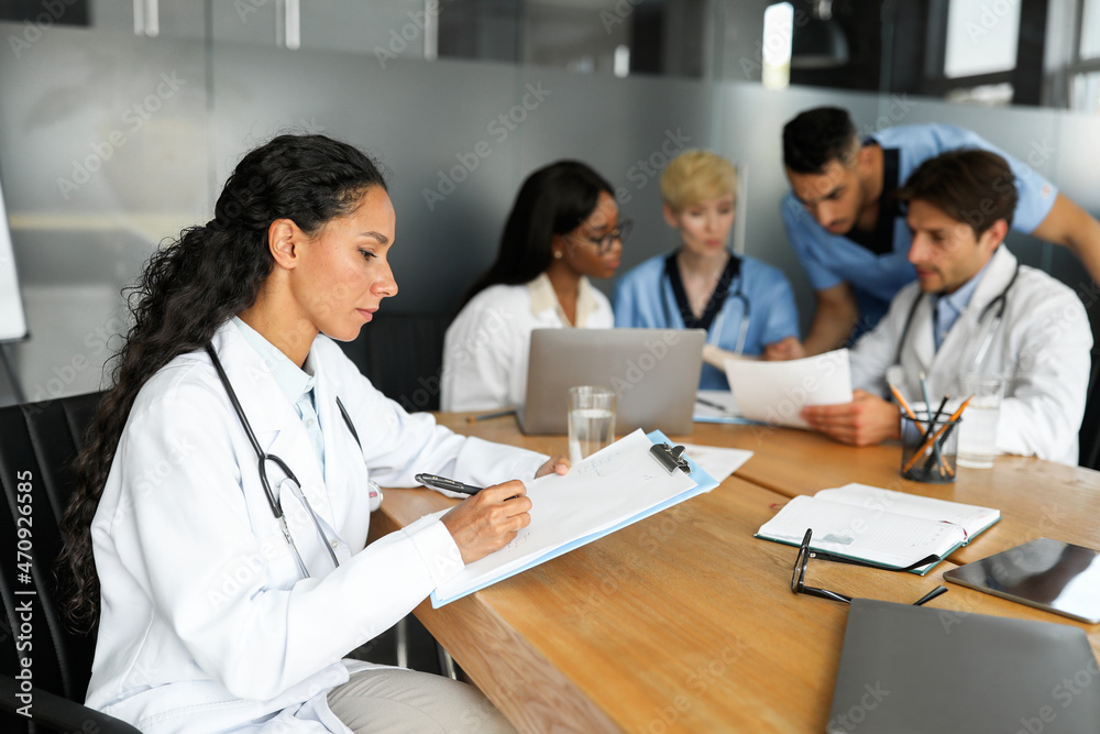 Concentrated multiethnic team of physicians sitting at table, having conversation Concentrated multiethnic team of physicians sitting at table, having conversation