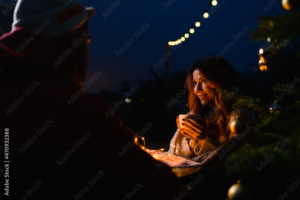 Girl with a cup of hot drink sits outdoors by the Christmas tree