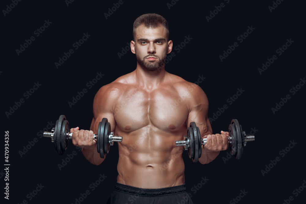 Front view of strong athletic man lifting dumbbells looking at camera isolated over black background Front view of strong athletic man lifting dumbbells looking at camera isolated over black background